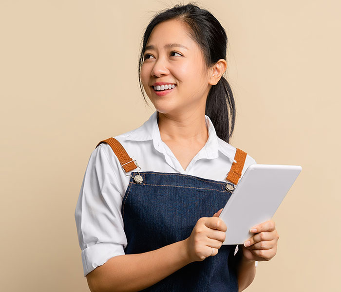 Young woman in ponytail wearing a workman's apron and holding a tablet