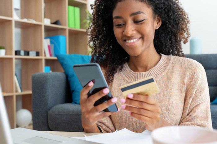 Young adult in a library holding a phone in one hand and a credit card in the other